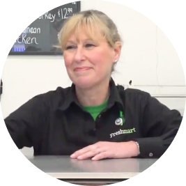 Smiling Freshmart employee with blonde hair sitting at a table.