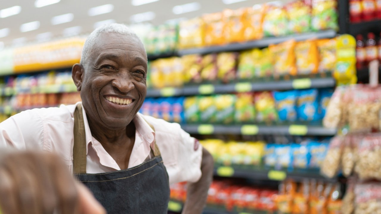 Freshmart employee leaning on shelves smiling.