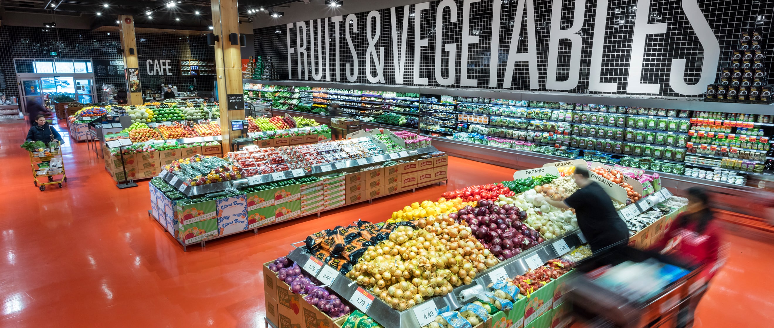 Fruits and vegetables section of a grocery store with fresh produce and people shopping.