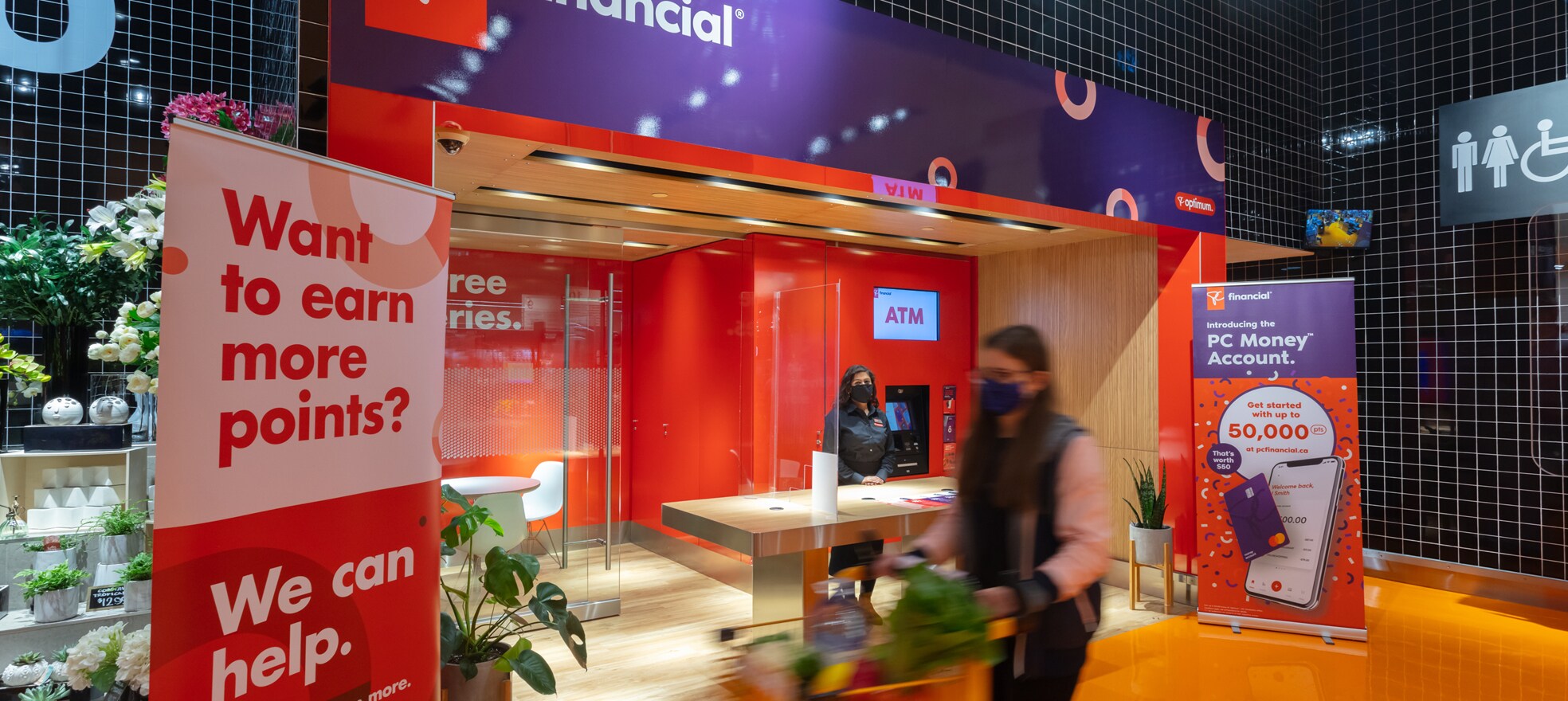 PC Financial employee wearing a mask standing behind a desk in a PC Financial area. 