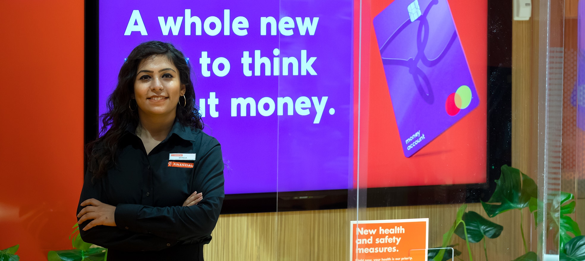 PC Financial employee standing with her arms across in front of a PC Financial ad on a screen.