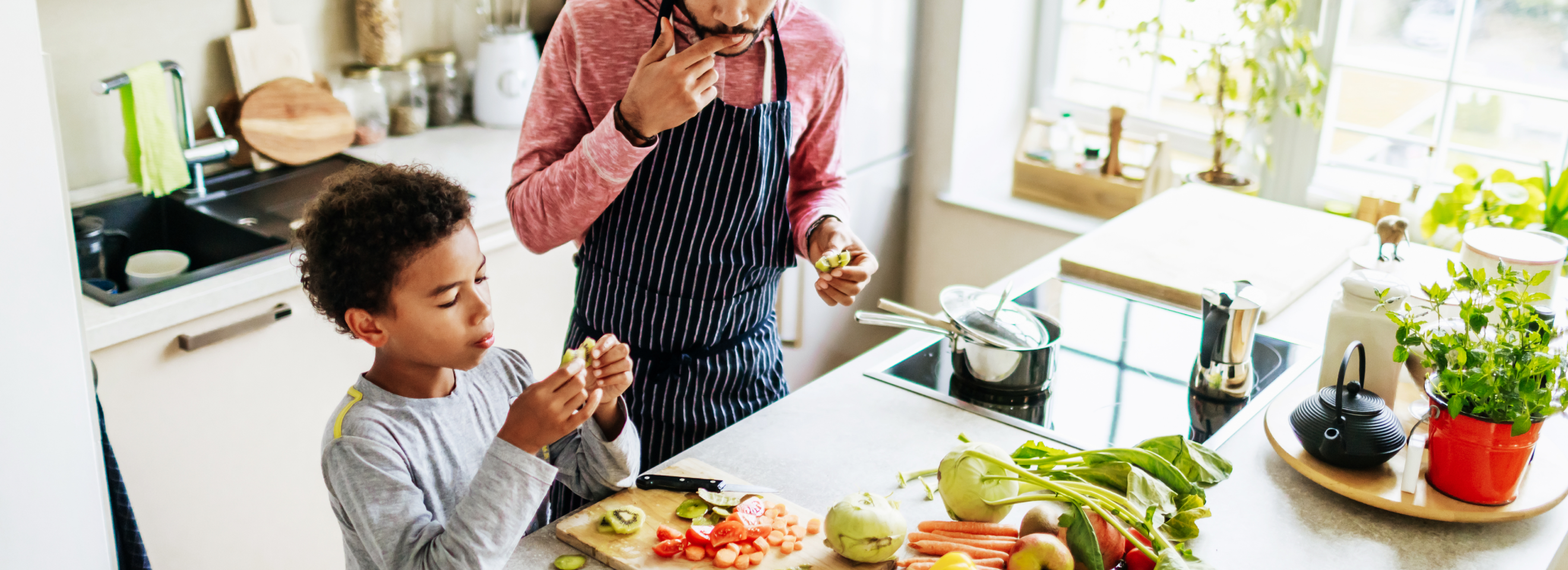 Man and son cooking together in brightly lit kitchen.