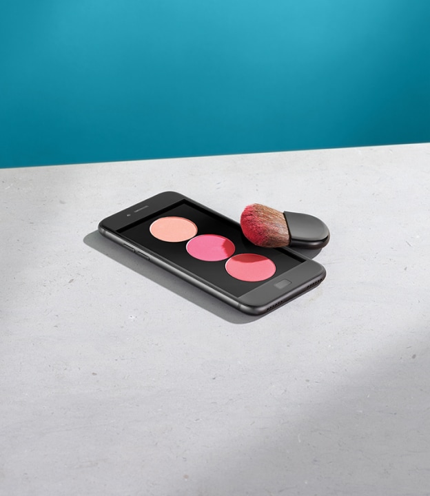 Une palette de fards à joues de trois teintes de rose, représentée sur l’écran d’un iPhone avec un pinceau.