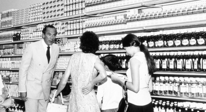 Murray Koffler en tailleur blanc s’adressant à une mère et à des enfants dans un magasin