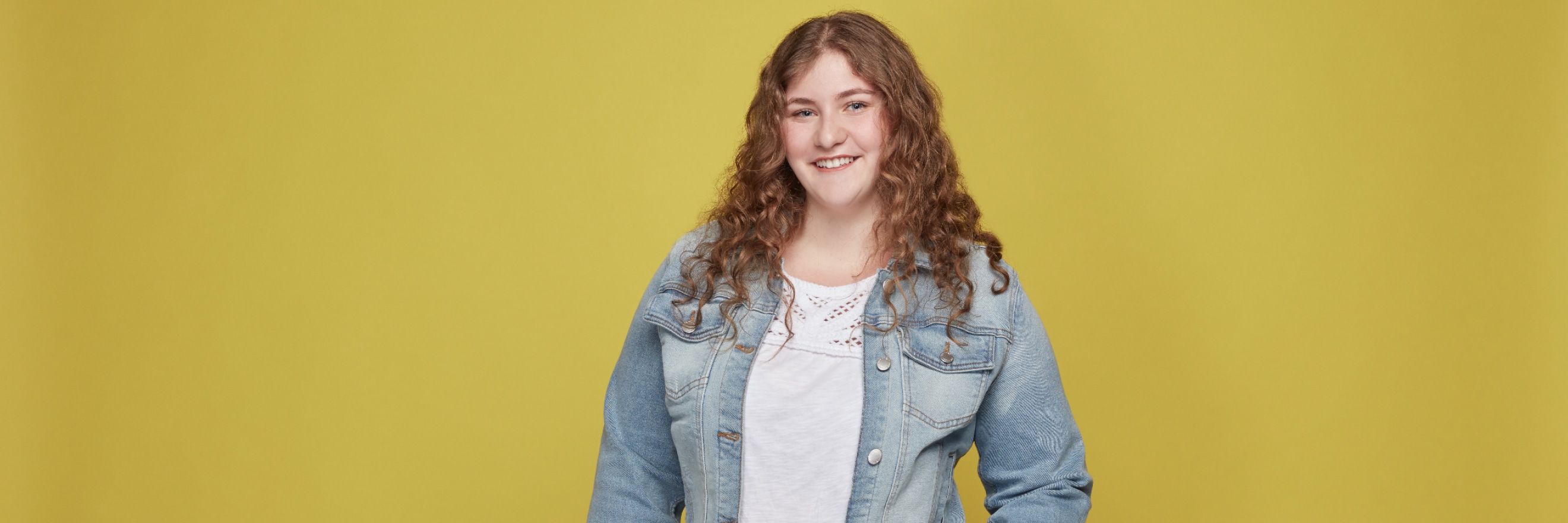 Young women in jean jacket smiling on a yellow background.