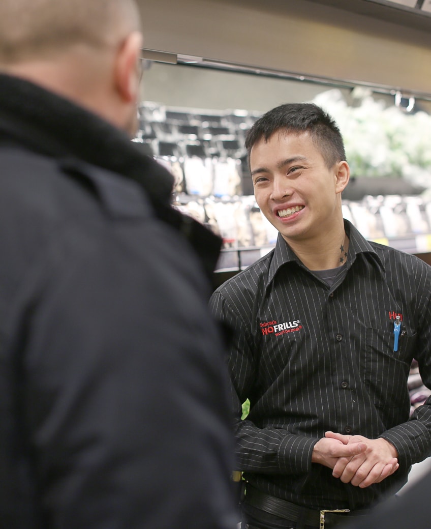 Smiling No Frills employee helping customer.