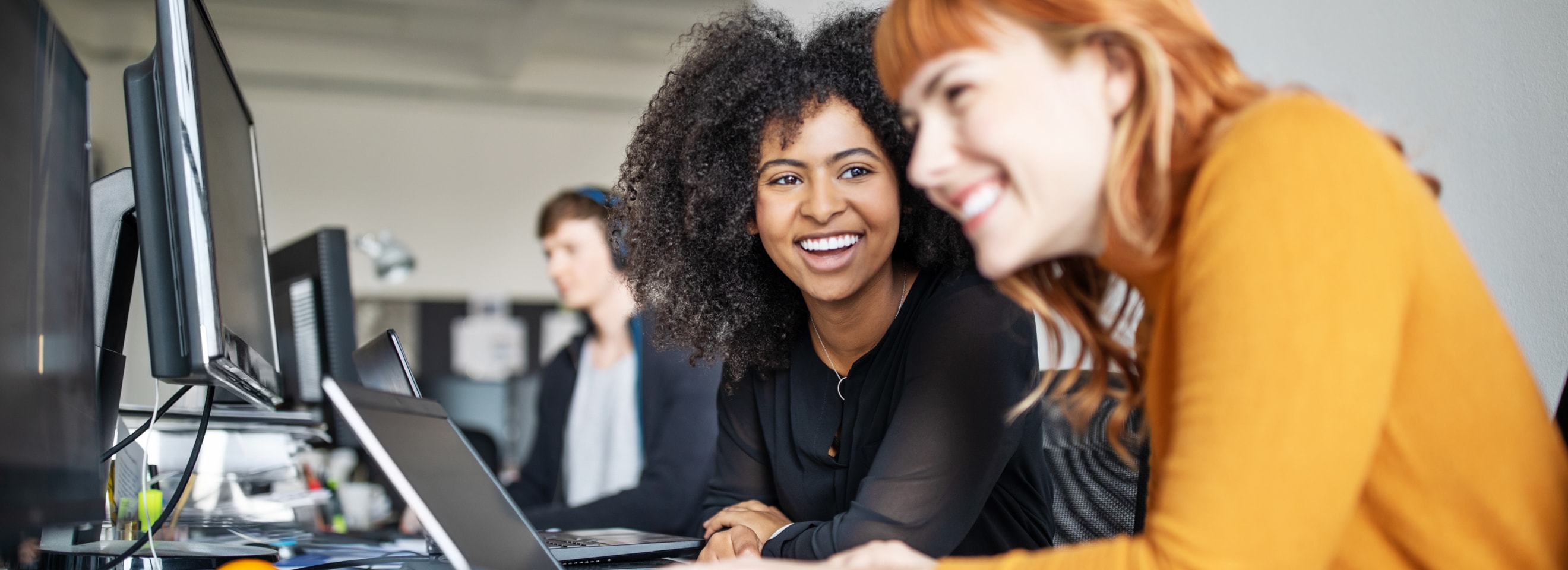 2 women colleagues smiling working in front of computers.