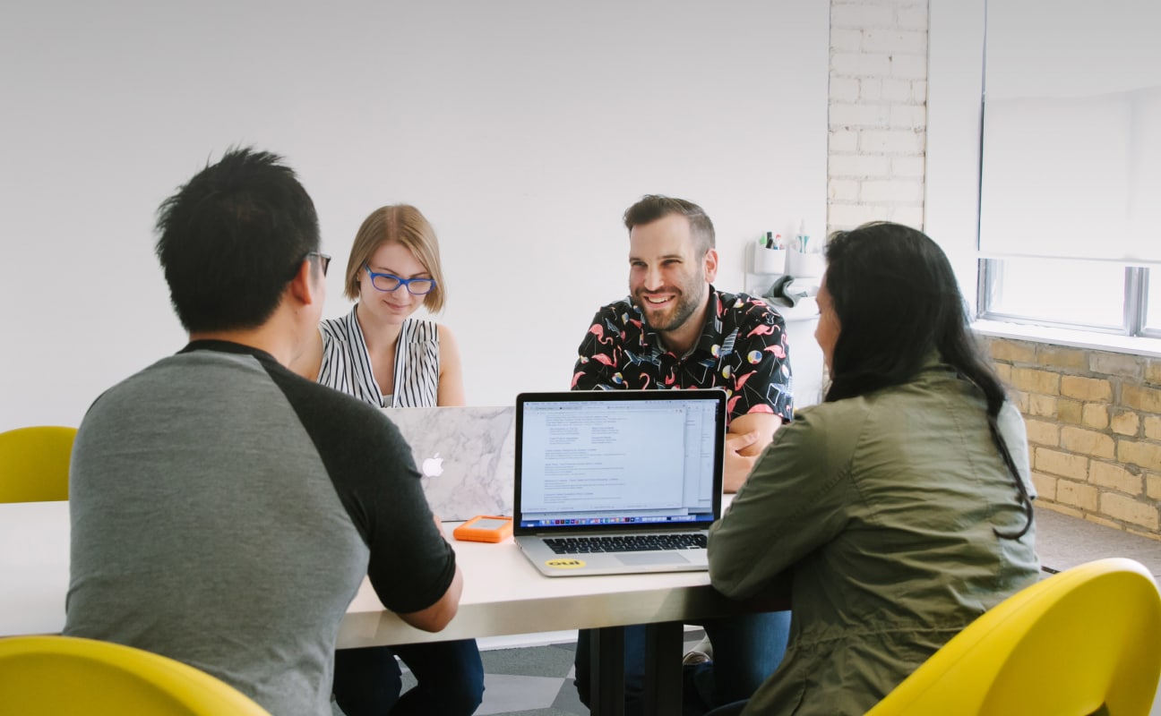 4 colleagues sitting in a brightly lit meeting room.