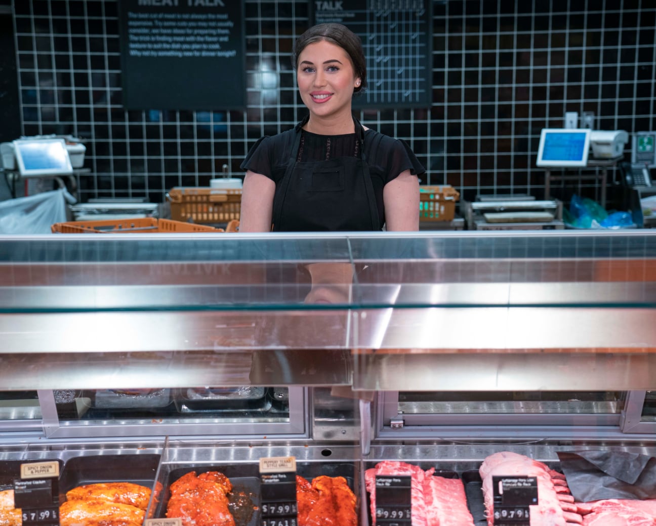 Jeune collègue souriant derrière un comptoir de viande dans une épicerie.
