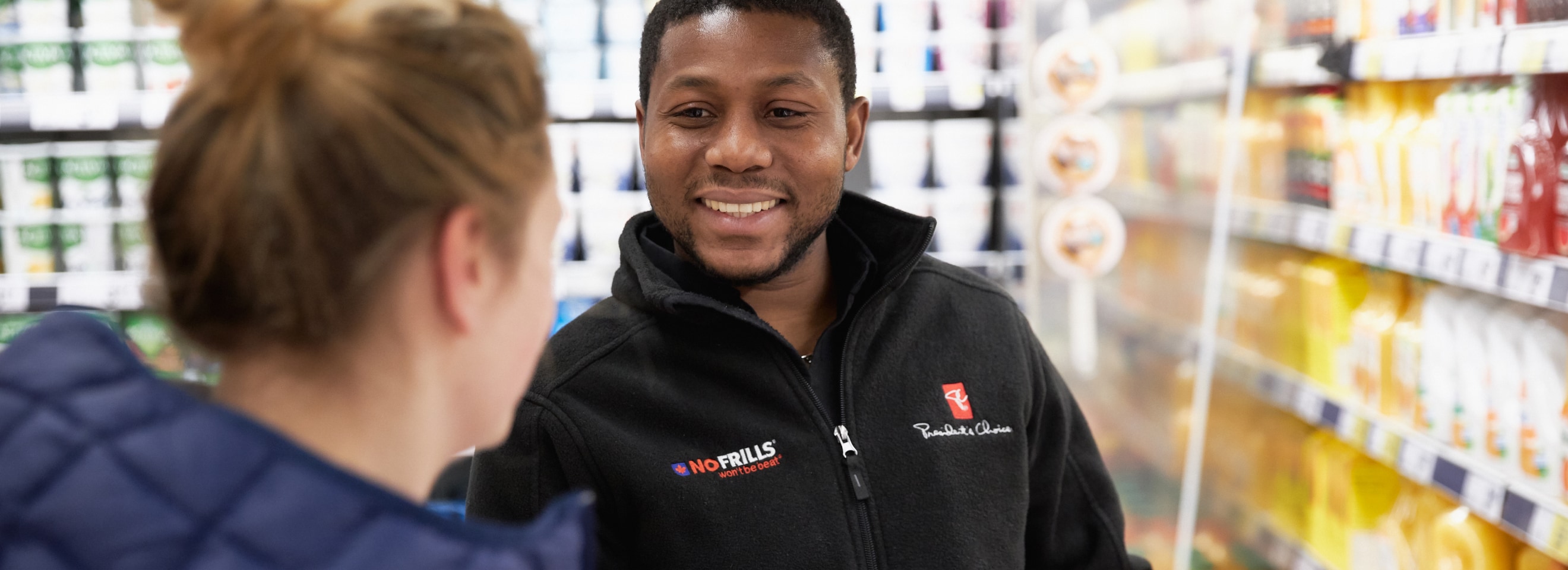 No Frills employee smiling and helping a customer.