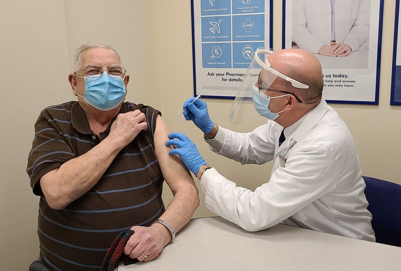 Shoppers Drug Mart Associate Owner Tony Alm gives the store’s first COVID-19 vaccine to Eugene Bochon in Edmonton, AB