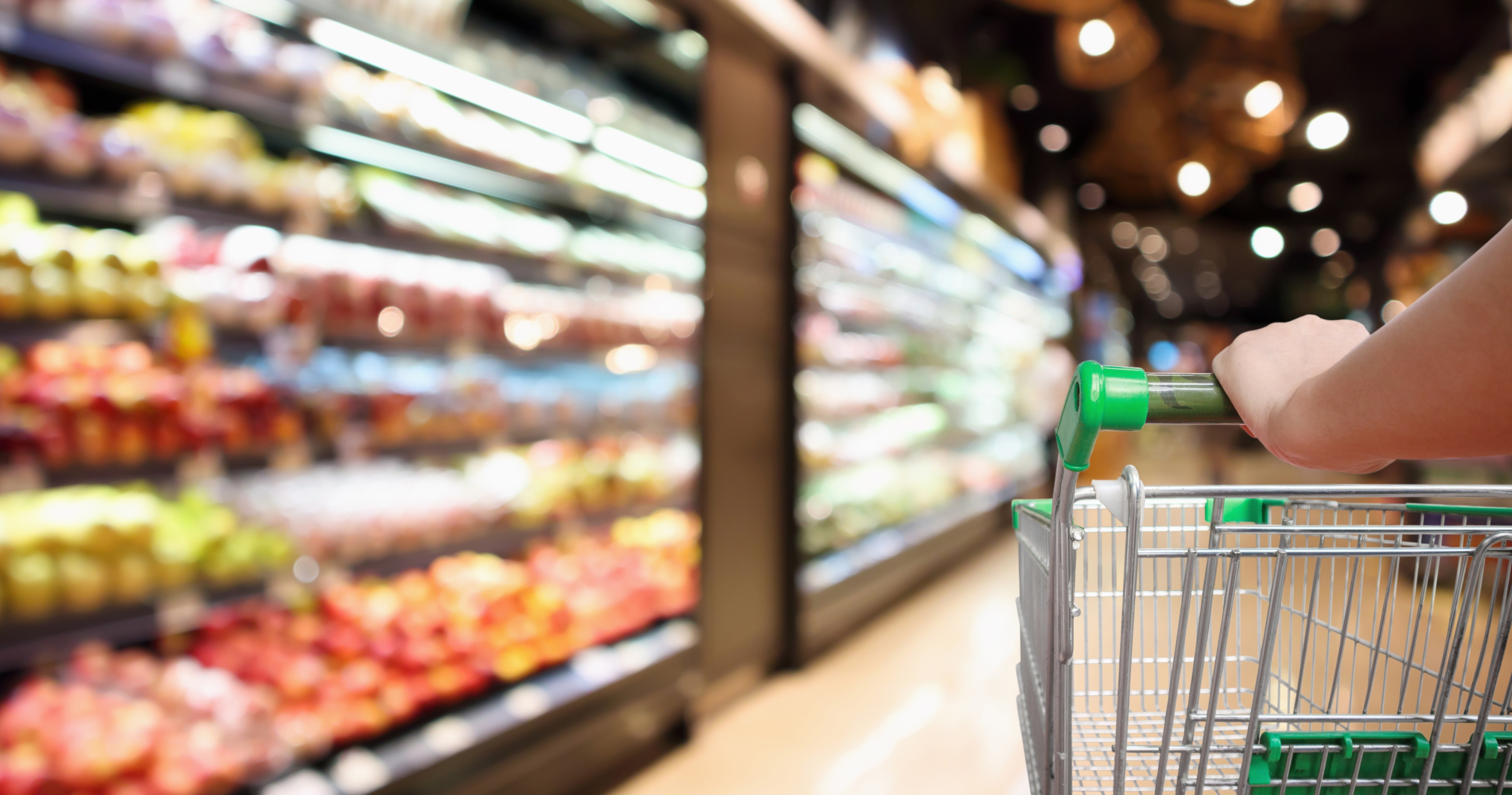 A person pushes a green shopping cart in a food aisle of a grocery store. 