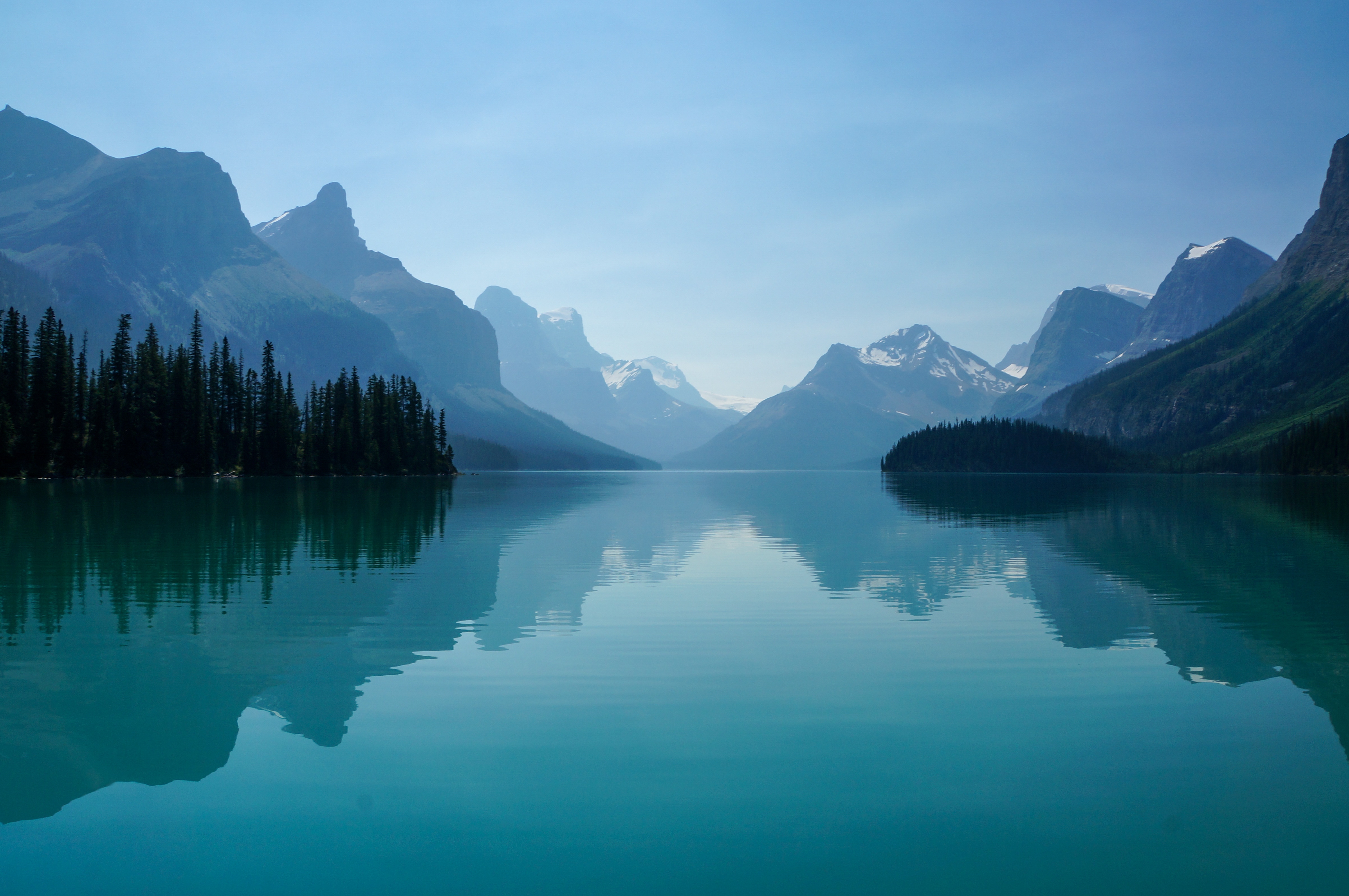 Un beau lac entouré d'arbres, de montagnes et d'un grand ciel bleu.