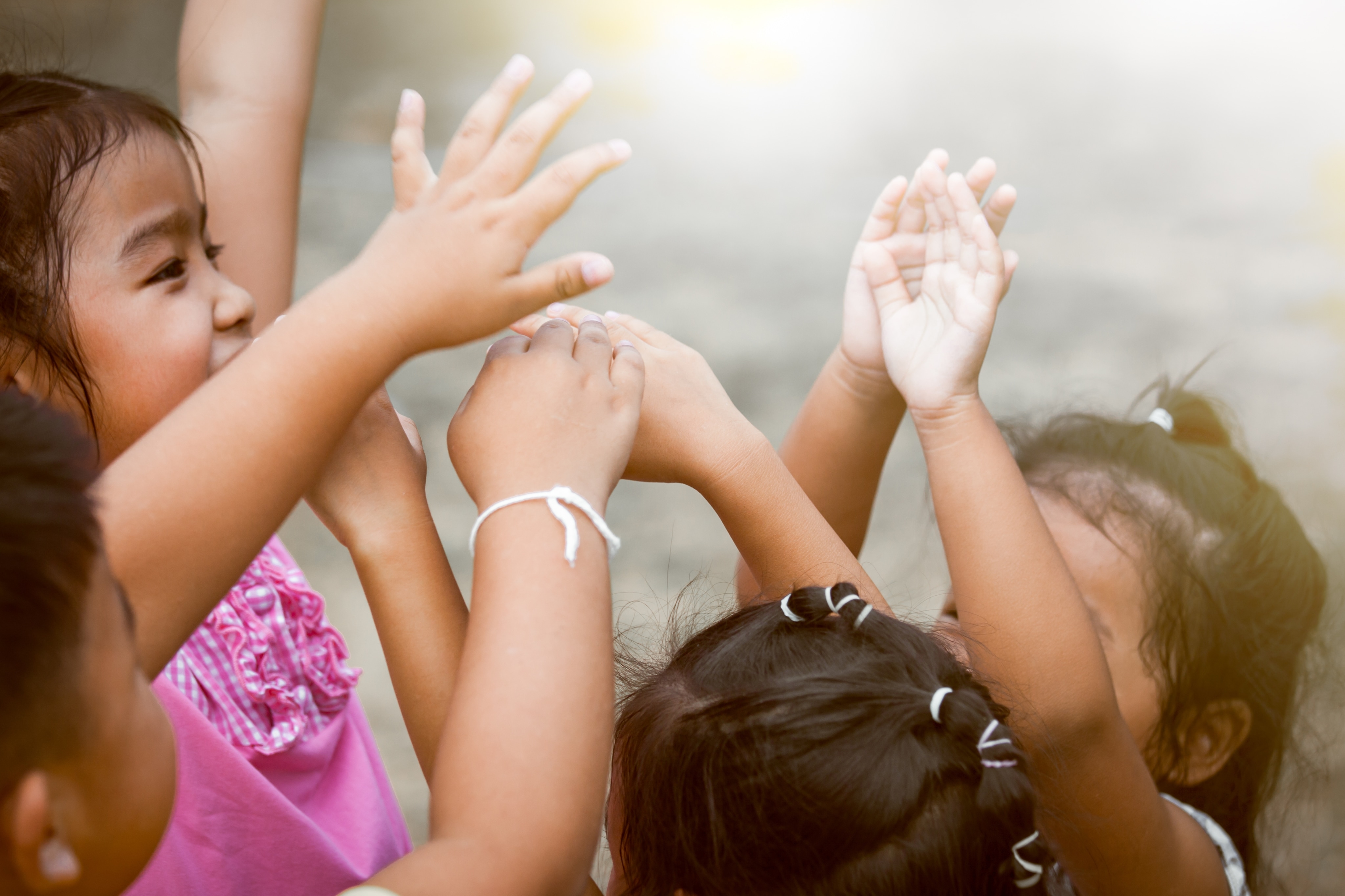 Quatre jeunes enfants racisés lèvent ensemble les mains en l’air. 