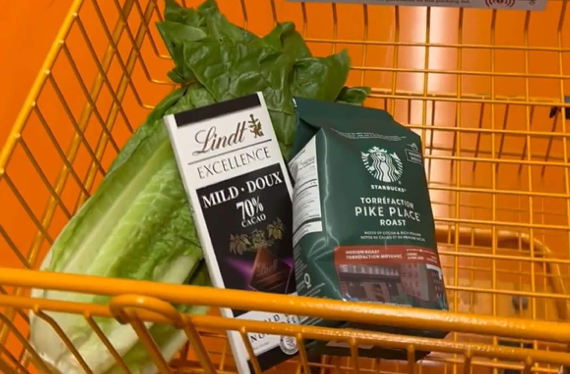 An orange shopping cart containing lettuce, a chocolate bar, and a bag of coffee.