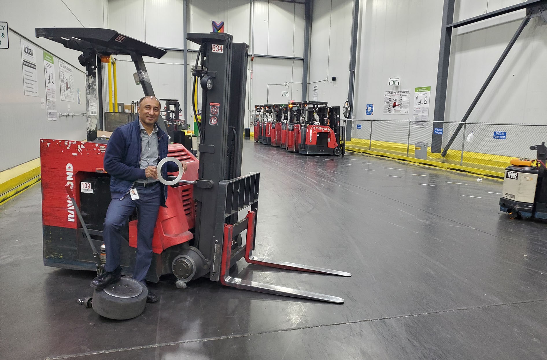 Adarsh kneels next to a loading machine holding the deflector piece he designed.