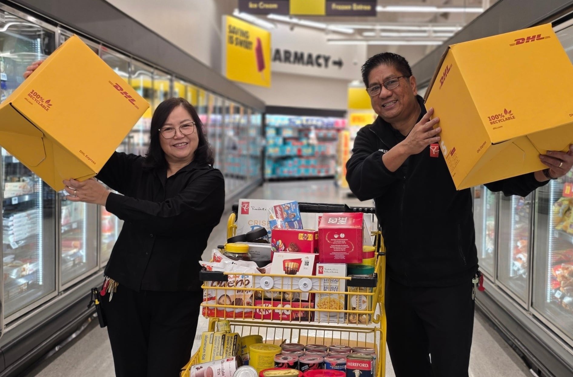 Une photo d'Emiliano et Anna tenant des boîtes de livraison au milieu d'une allée d'épicerie, avec un panier rempli de produits alimentaires devant eux.