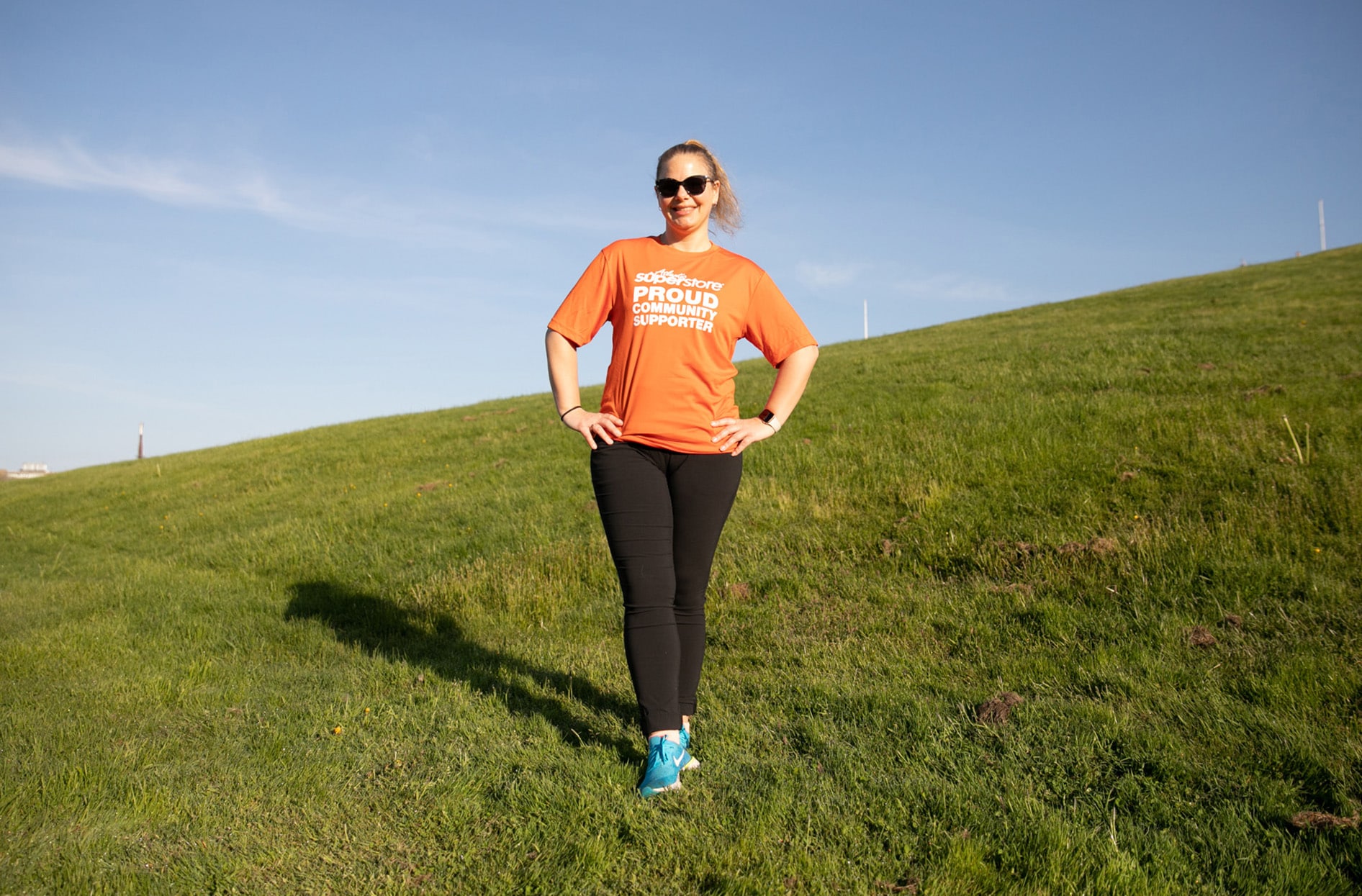 Belinda stands outside on the field smiling while wearing an orange Atlantic Superstore shirt that says, “Proud Community Supporter.”