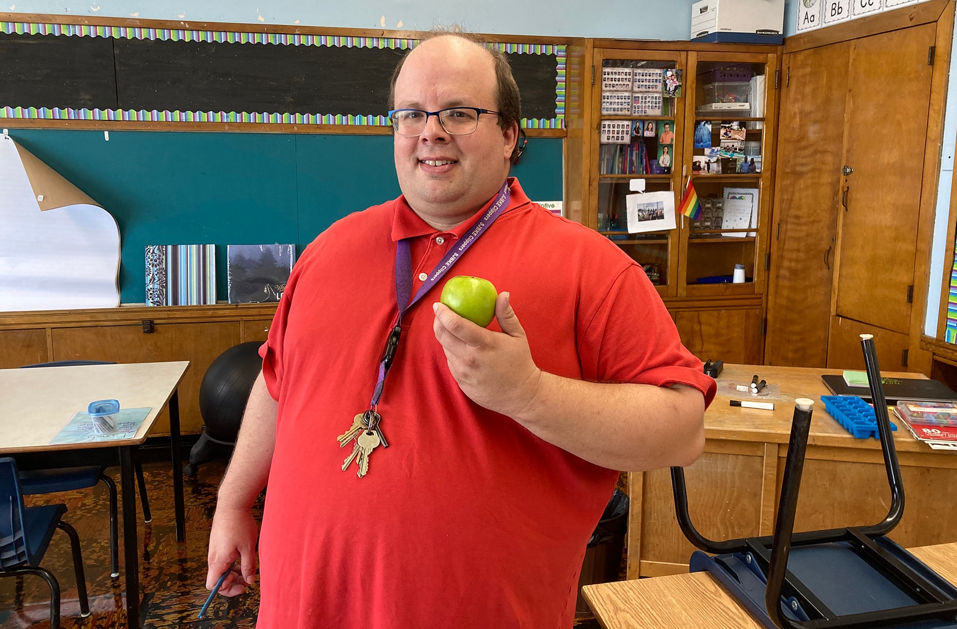Ben stands inside a classroom inside his school holding an apple.
