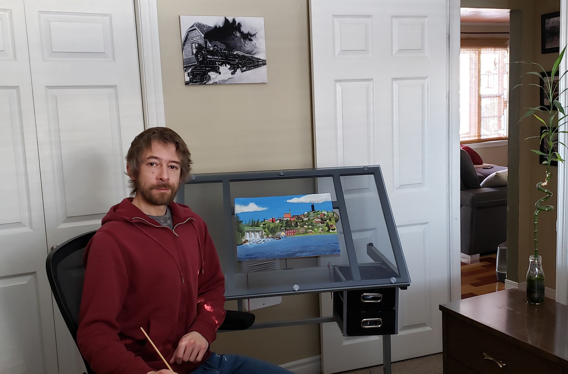 Brad sits in front of his painting easel at home.