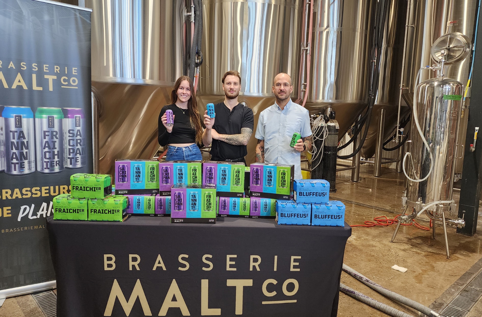 Les employés de la microbrasserie Brasserie Maltco posant avec leurs produits de bière à la main 