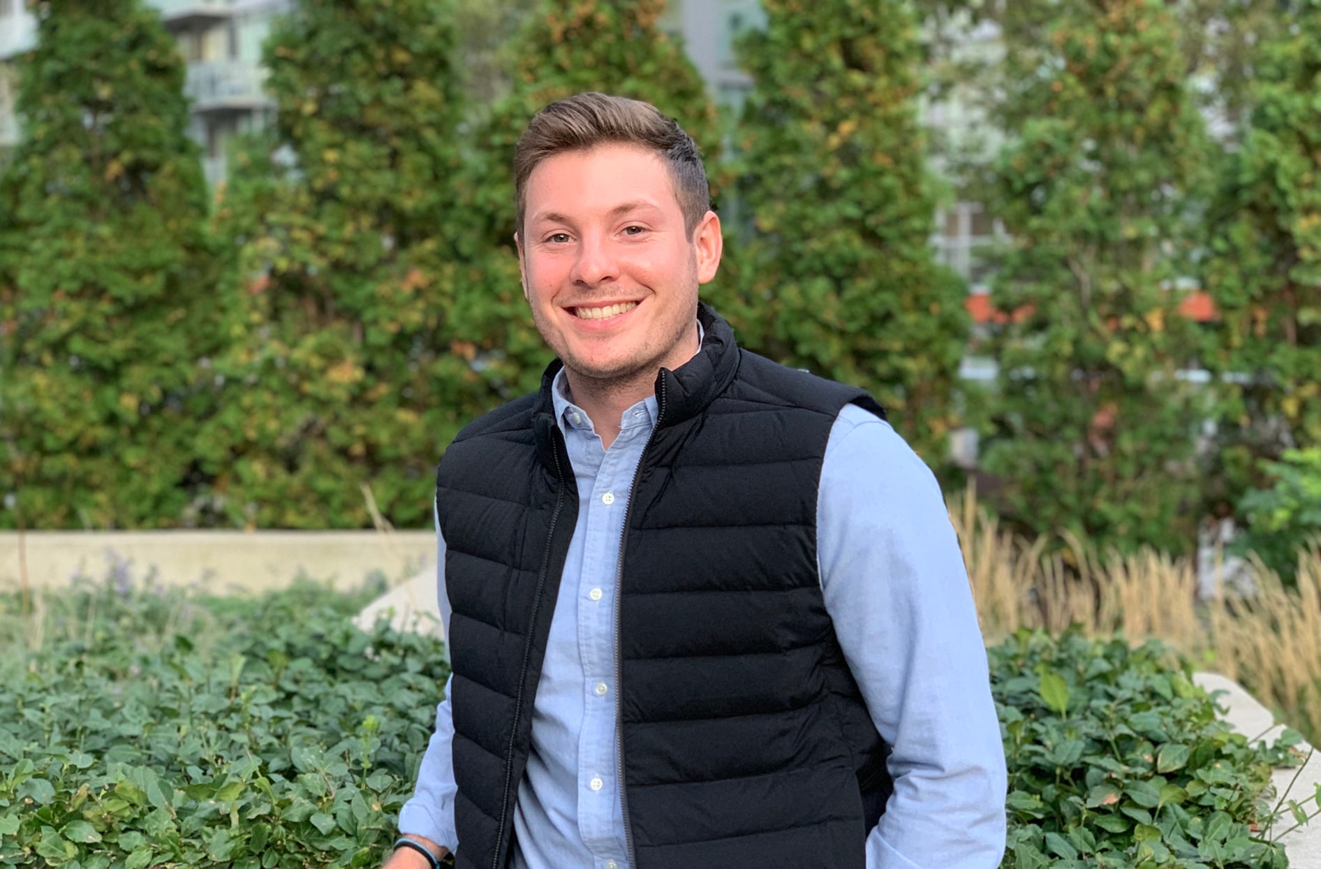 Brian stands in front of a garden smiling. 