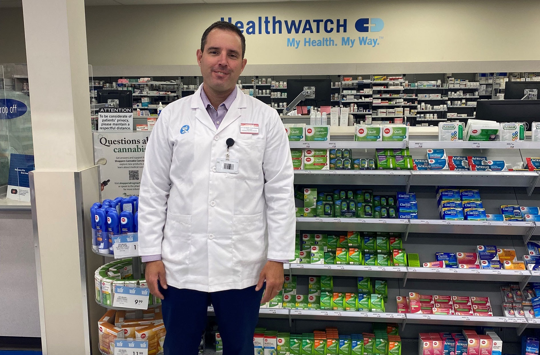 Bryce stands in front of the pharmacy counter at Shoppers Drug Mart smiling