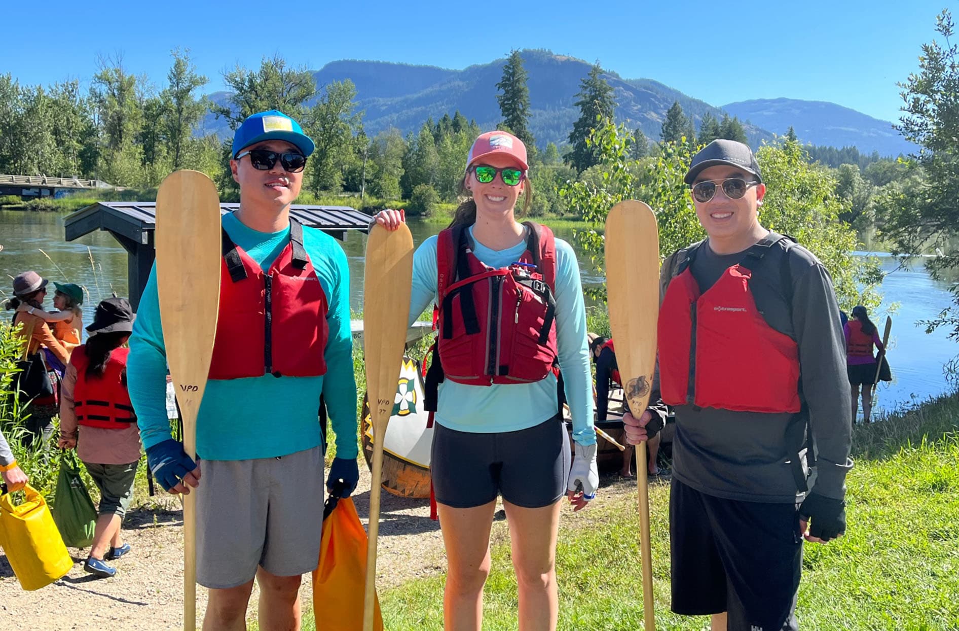 Kim stands with Ed Chiu and Stephen Tam outside holding canoe paddles and wearing life jackets. 