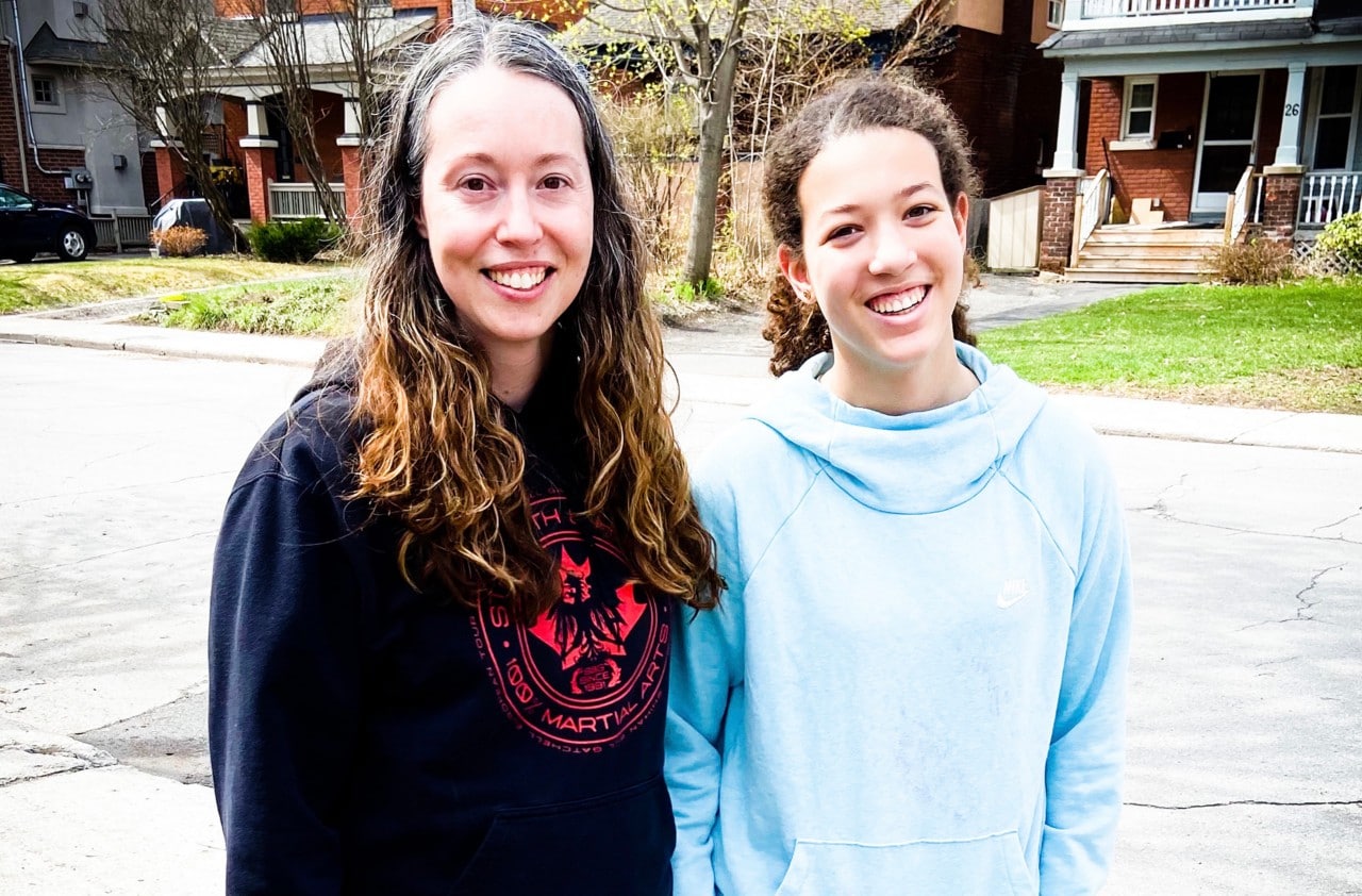 Une mère et sa fille adolescente souriantes, debout dans la rue de leur quartier 