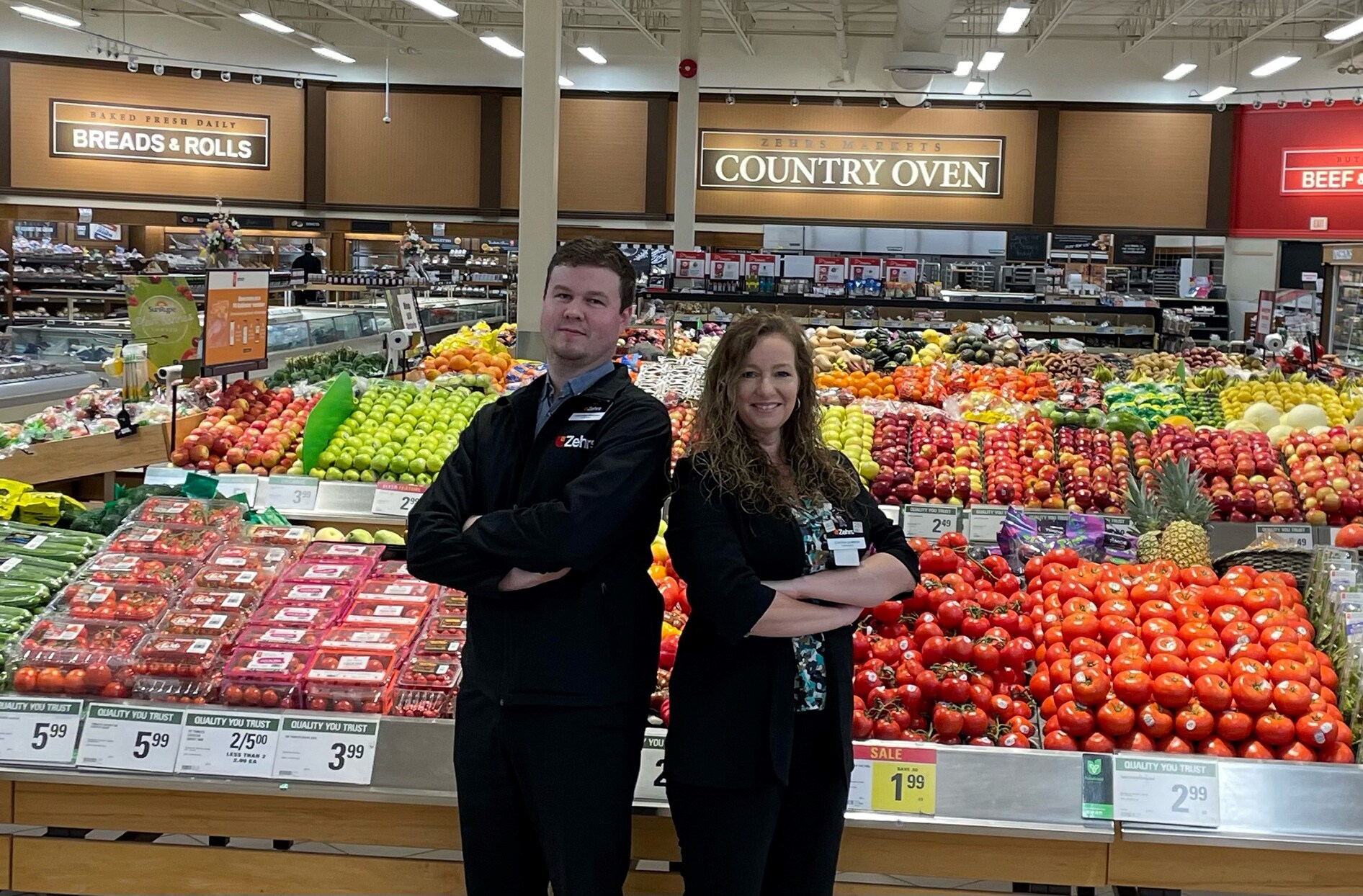 Cynthia et Luke se tiennent côte à côte à l’intérieur de leur magasin, devant les présentoirs de fruits. 