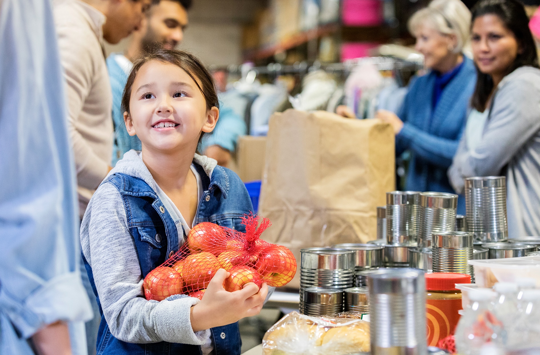 A young girl holds a bag full of apples, smiling. 