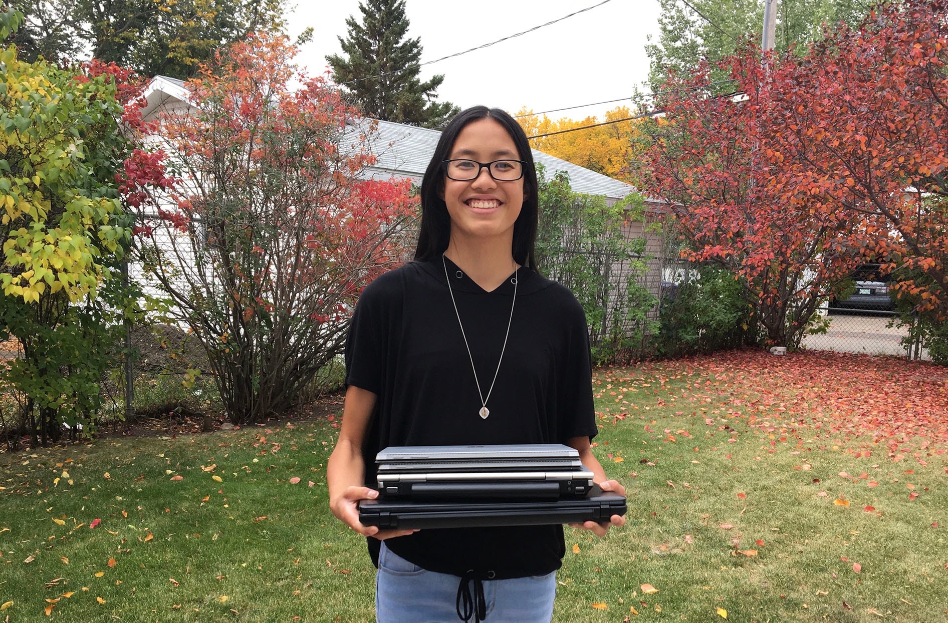 Emily smiles as she stands outside on the grass holding laptops in her hands