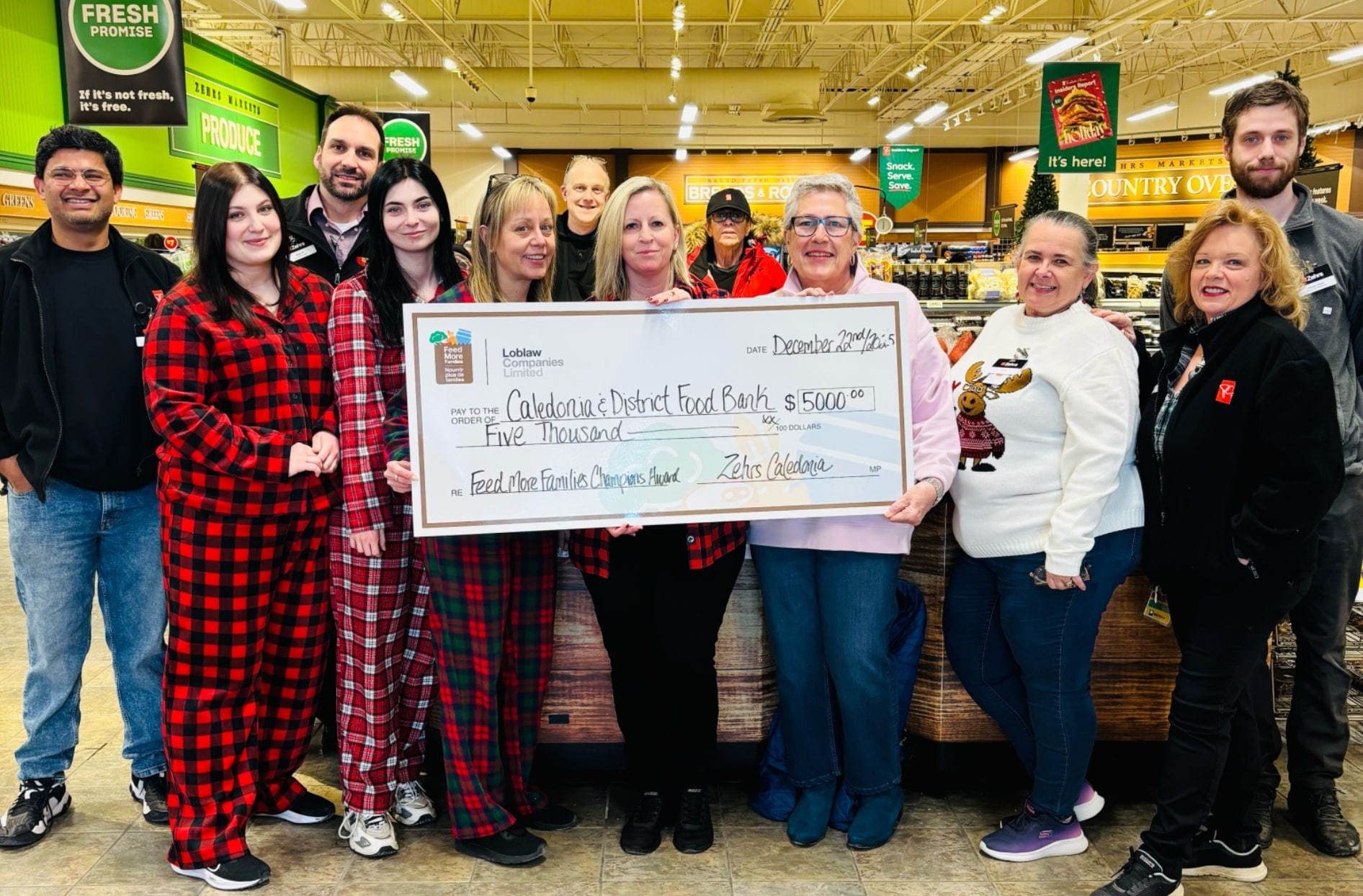 Un groupe d’employés d’épicerie se tient à l’intérieur d’un magasin en tenant un chèque des Champions Feed More Families.