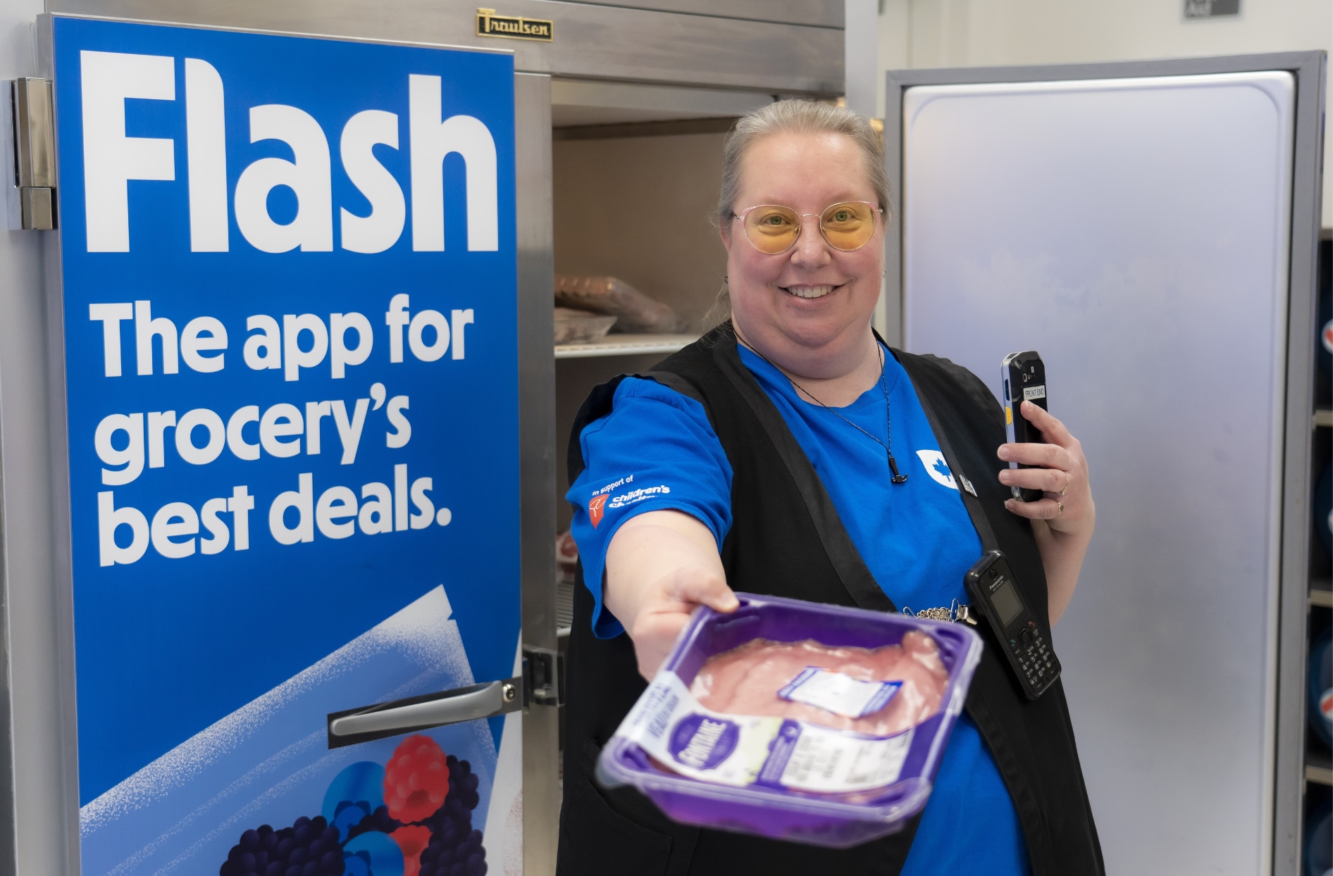 Une photo d’une collègue d’un Real Canadian Super Store qui tient de la nourriture dans sa main devant un réfrigérateur Flashfood. 