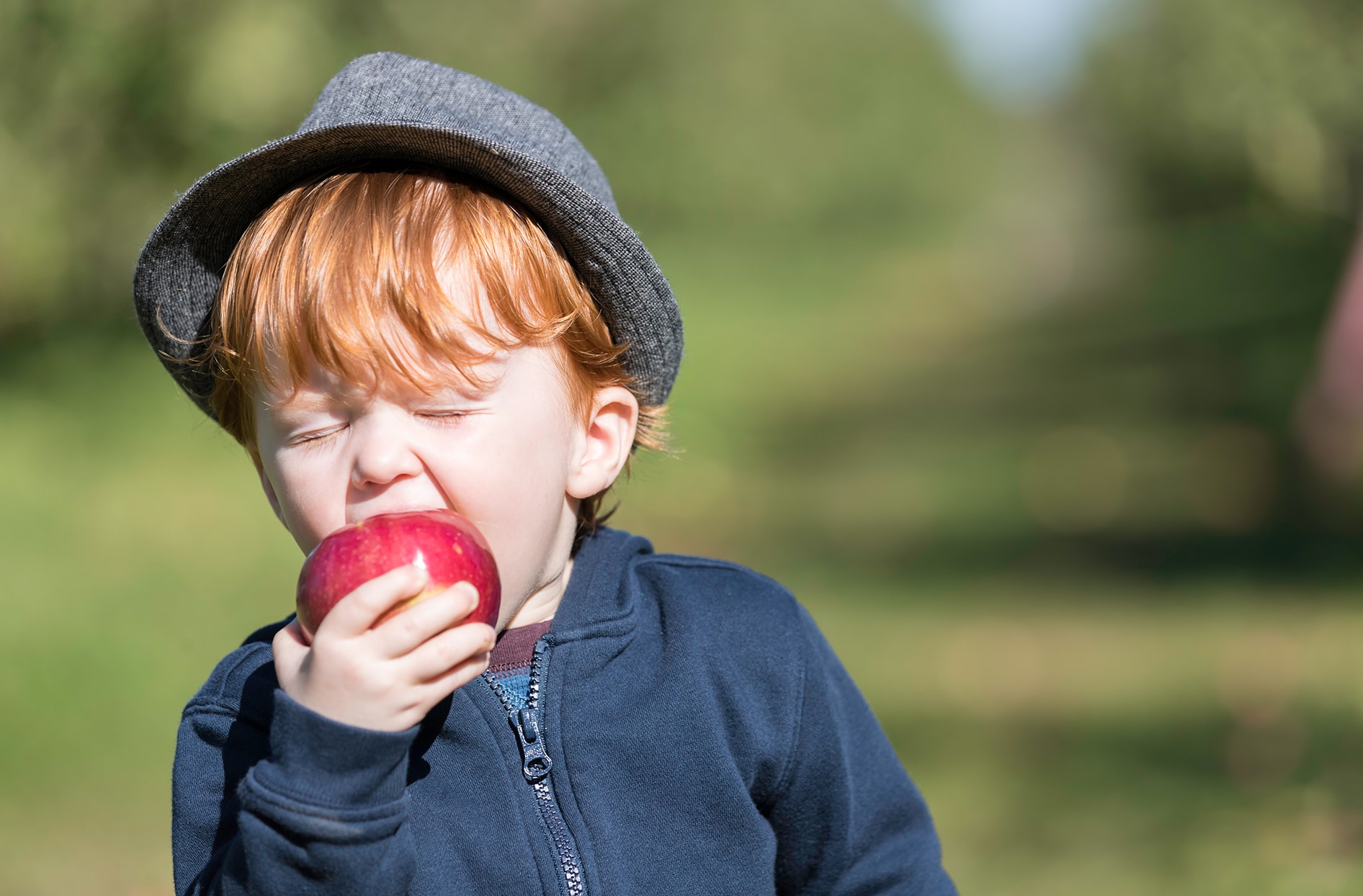 A little boy takes a big bite out of a red apple.