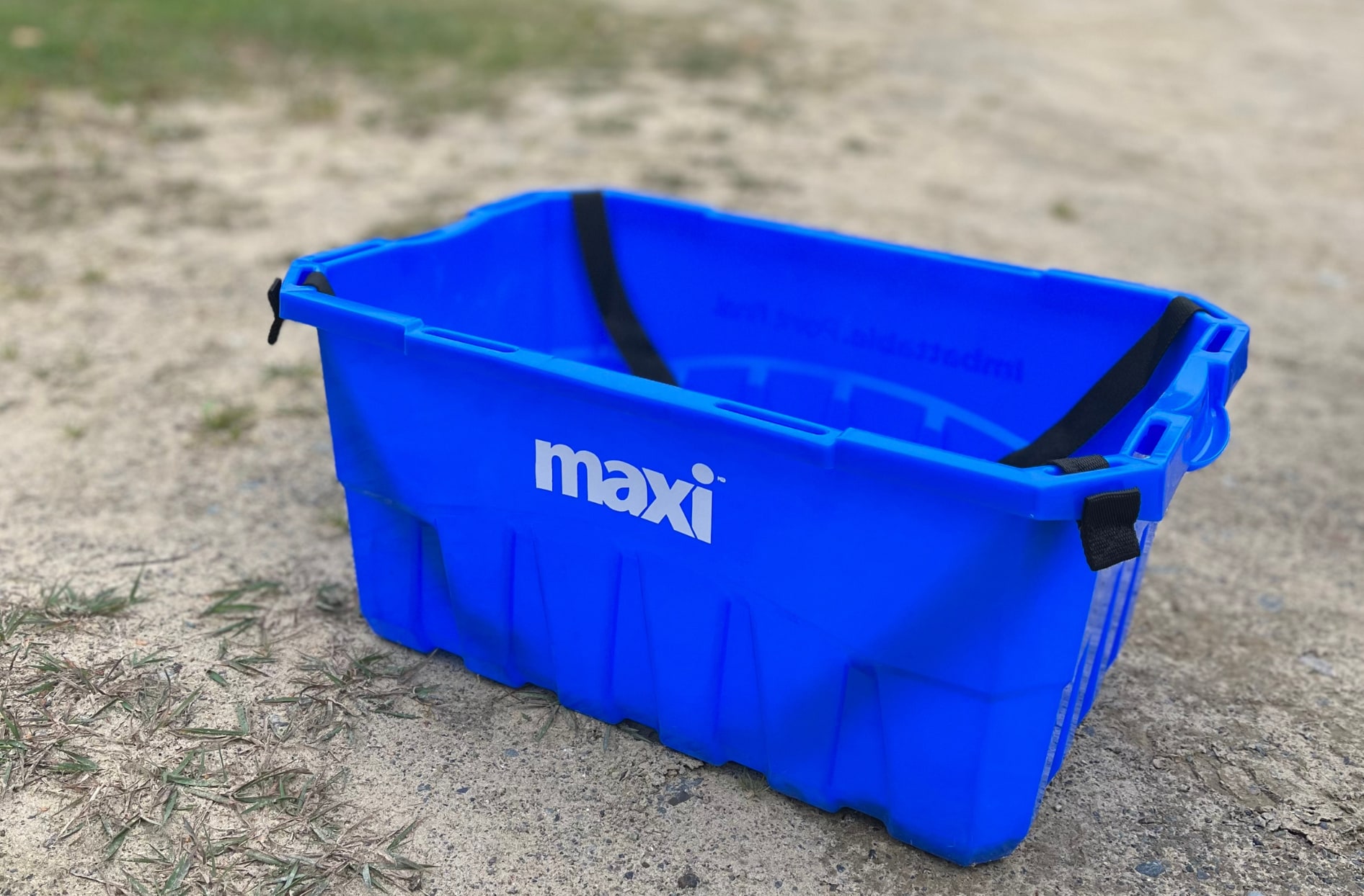 A photo of a blue reusable shopping basket with the maxi logo on the side sitting on sand outside.