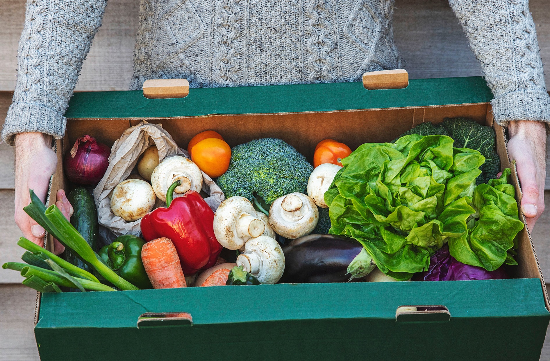 A man holding a cardboard box of fresh vegetables