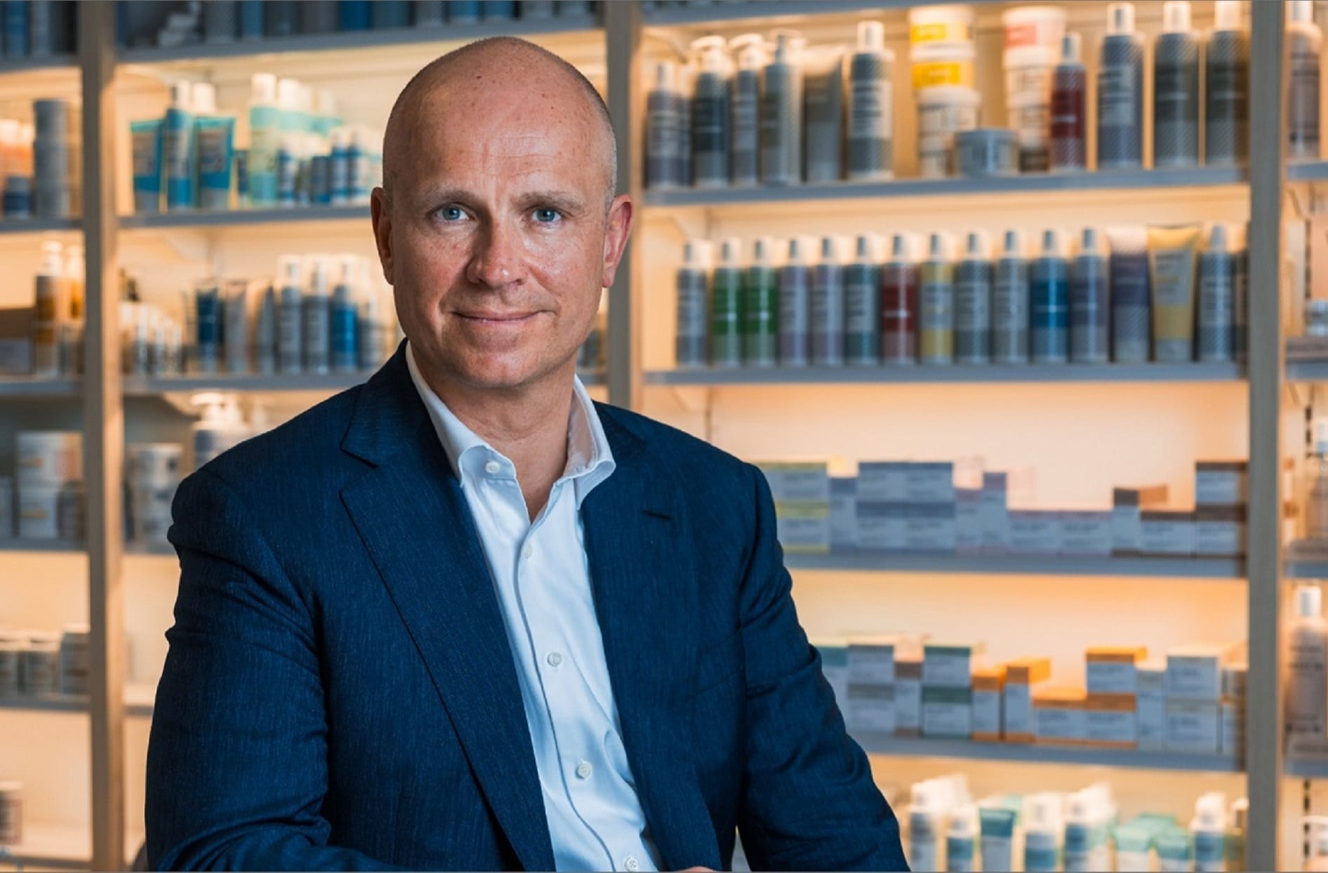 A headshot of Gregers sitting down smiling with products behind him in the background.