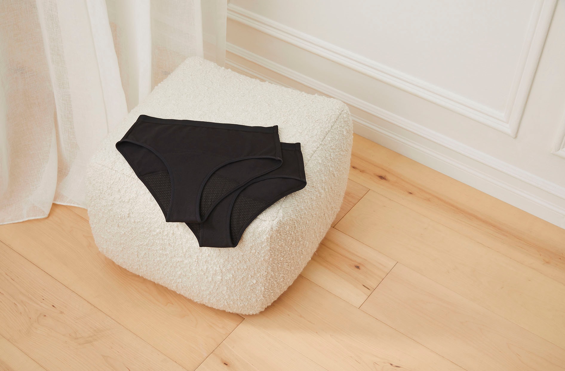 A picture of the underwear placed on a pouf in a light filled room. 