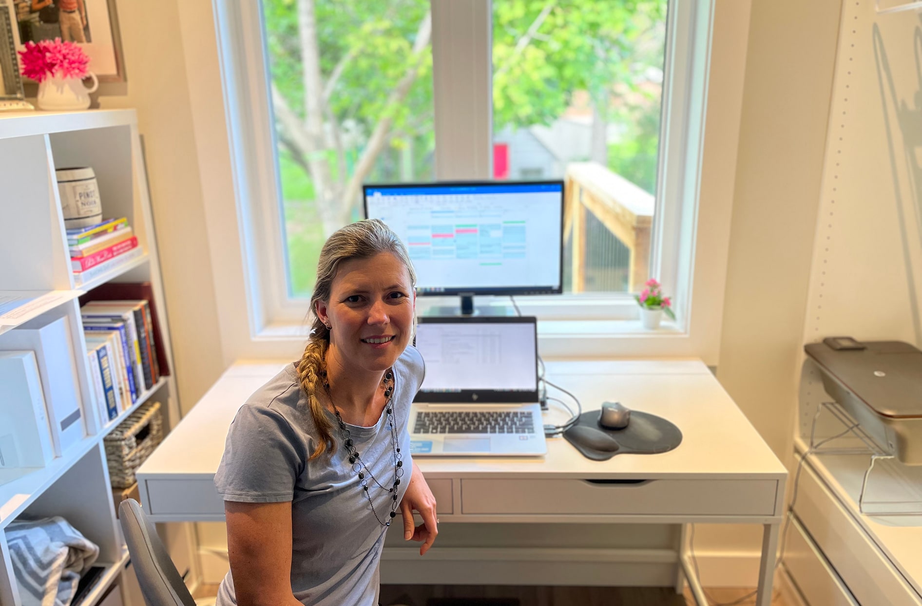 Jamie sits at her desk next to a big window, turned towards the camera and smiling