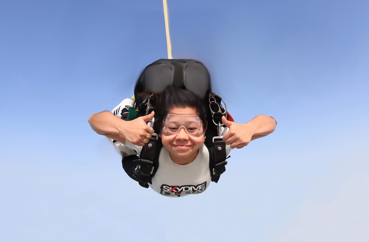 Smiling woman giving two thumbs up while skydiving