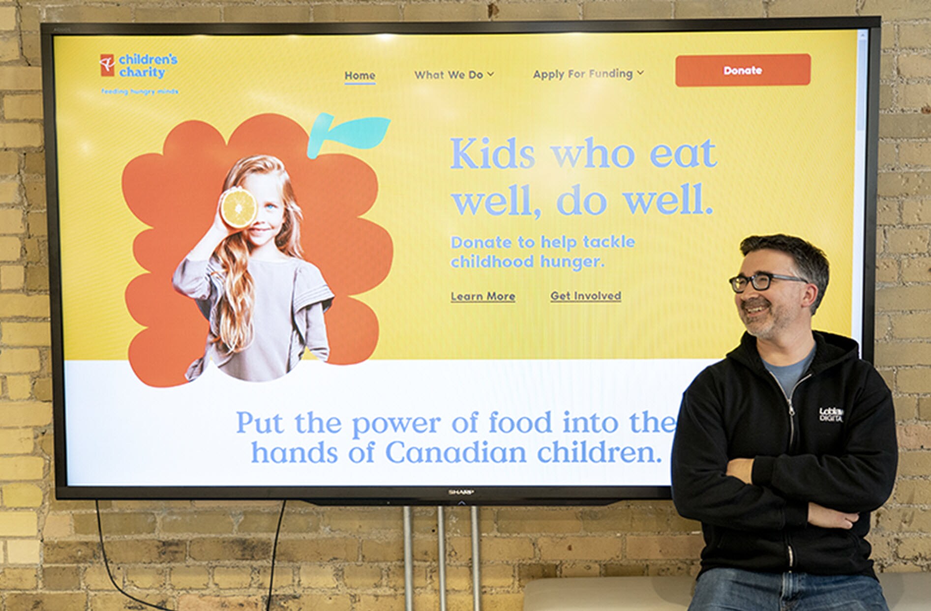 Jerrold stands in front of a large screen displaying the PC Children's Charity home page