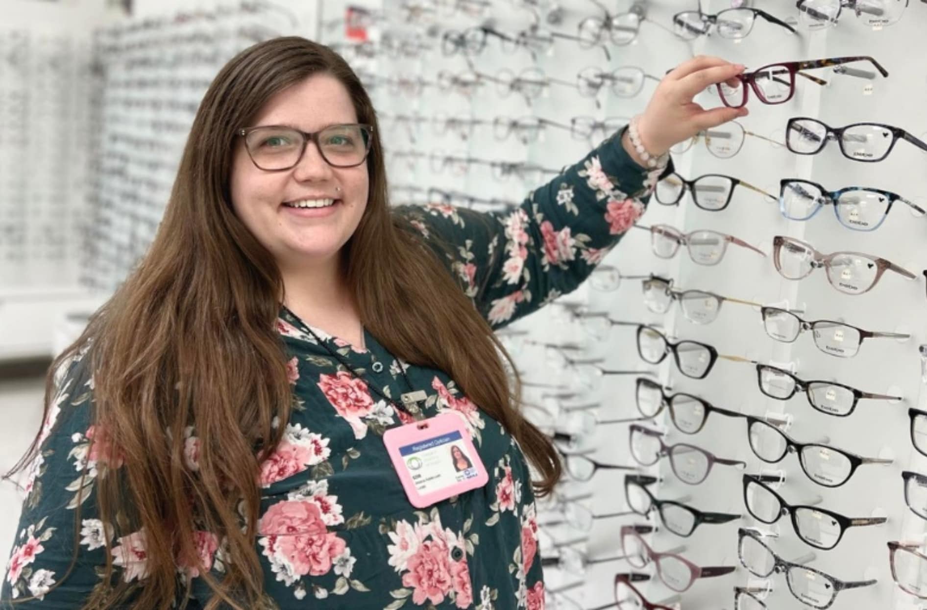 Jessica standing next to a display of eyeglasses, picking up a pair.