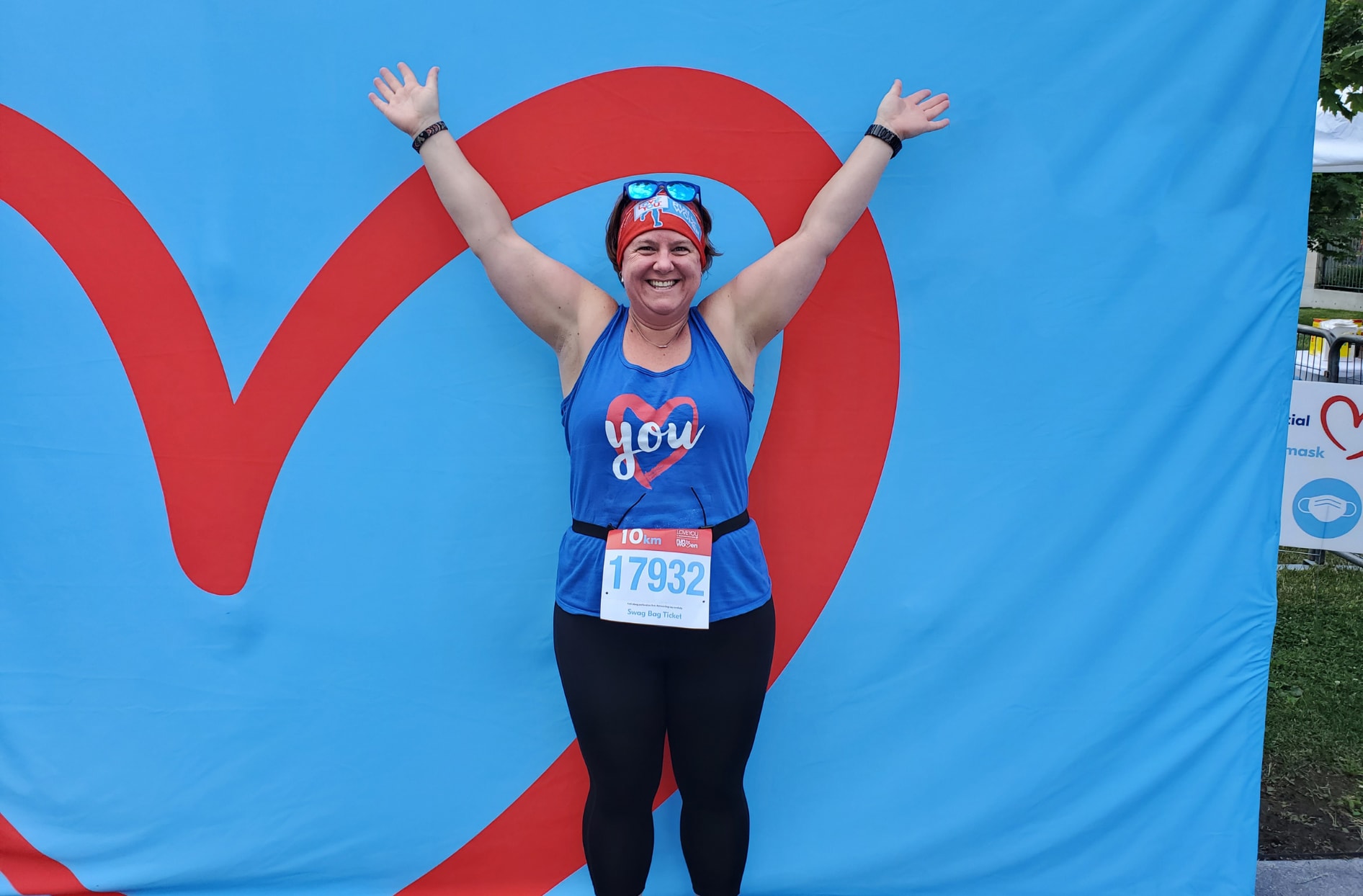 Jessica stands with her arms up in the air celebrating participating in a Run for Women event.  