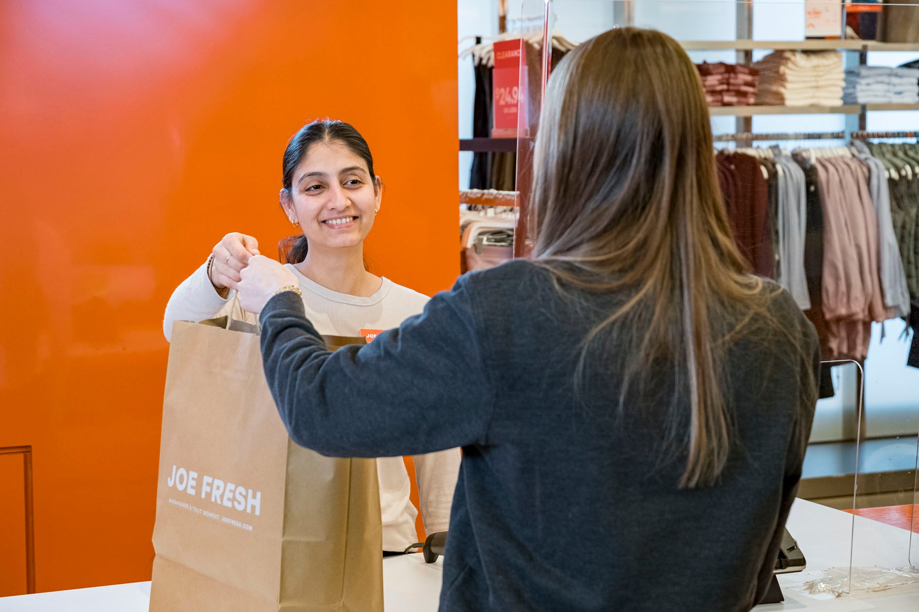 A picture of a customer purchasing something at the checkout holding a Joe Fresh recyclable bag. 