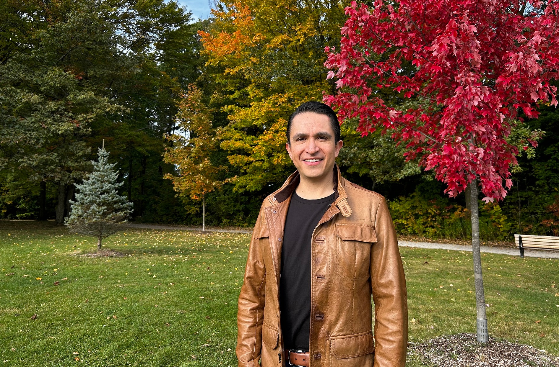 Jorge stands outside with colourful trees behind him. 