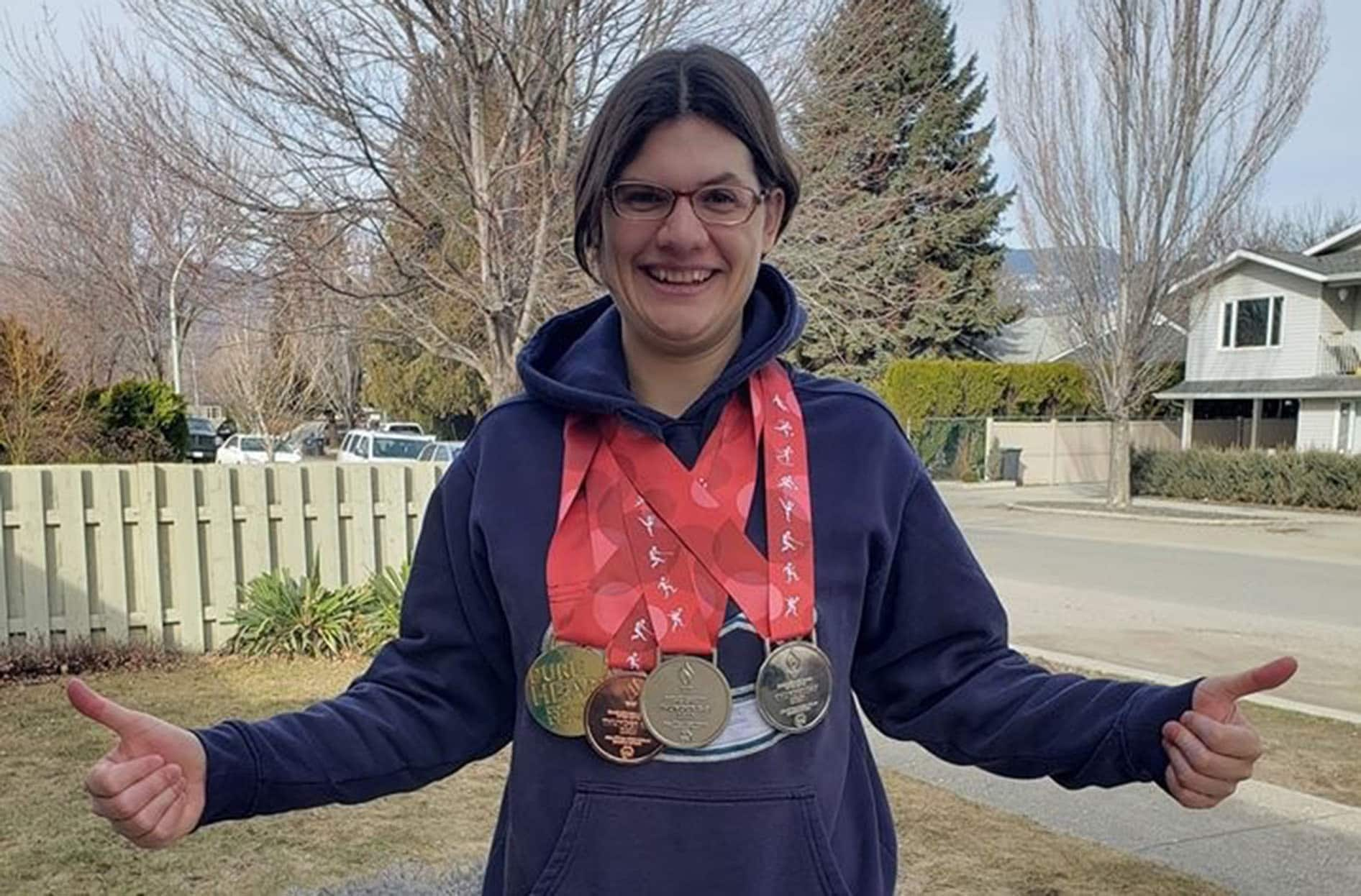 Kelsey est debout à l’extérieur, les pouces levés, et sourit avec ses médailles autour du cou