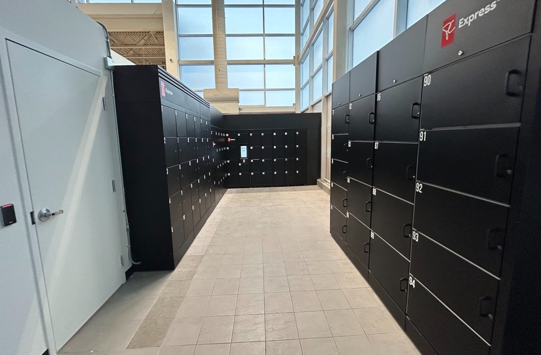 Un espace de casier intérieur lumineux avec des rangées de casiers intelligents PC ExpressPC noirs alignés sur les deux côtés et sur le mur arrière. Chaque porte de casier est numérotée.