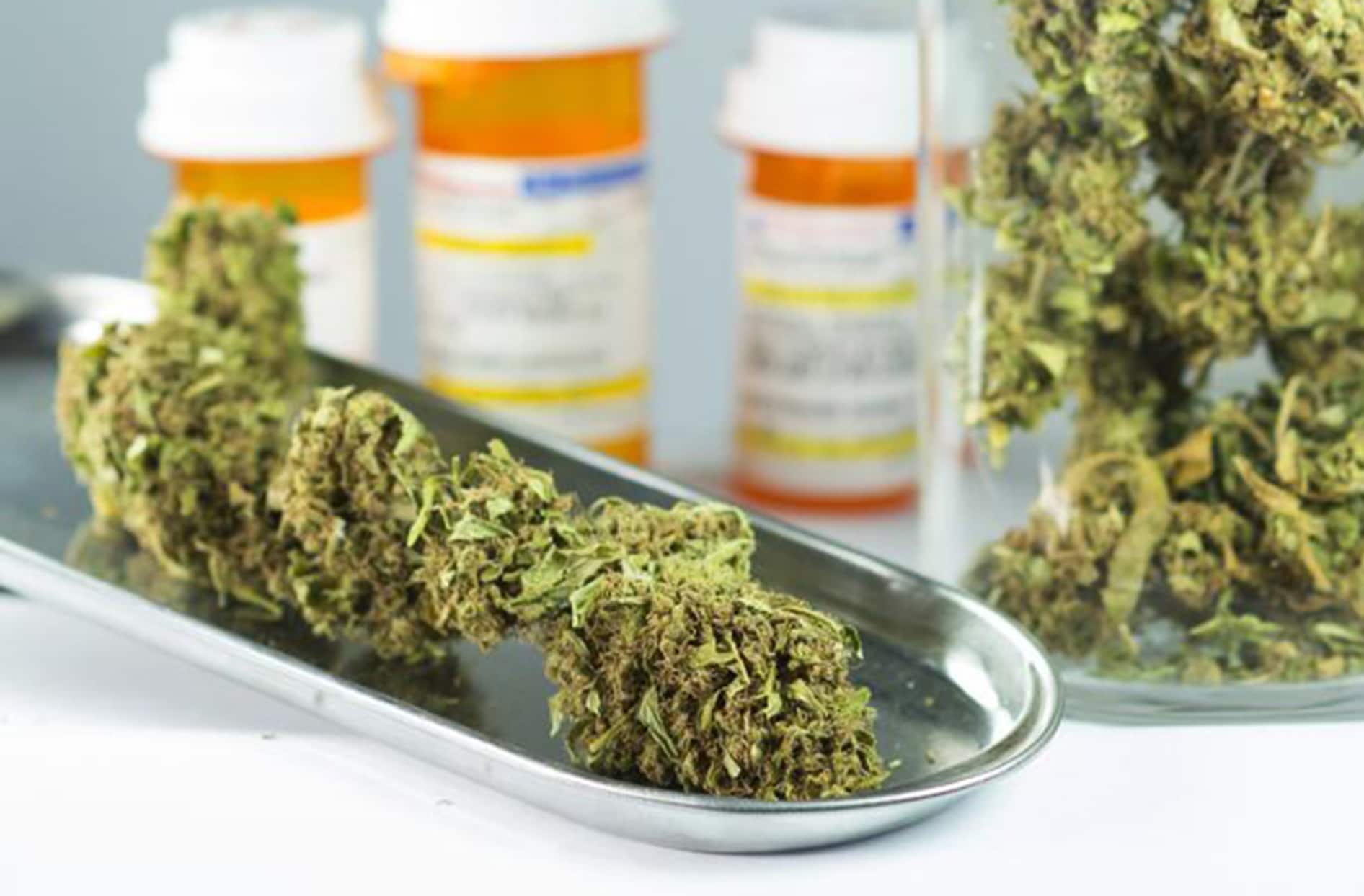 Medical cannabis sits on a metal tray and in a glass jar with prescription bottles in the background