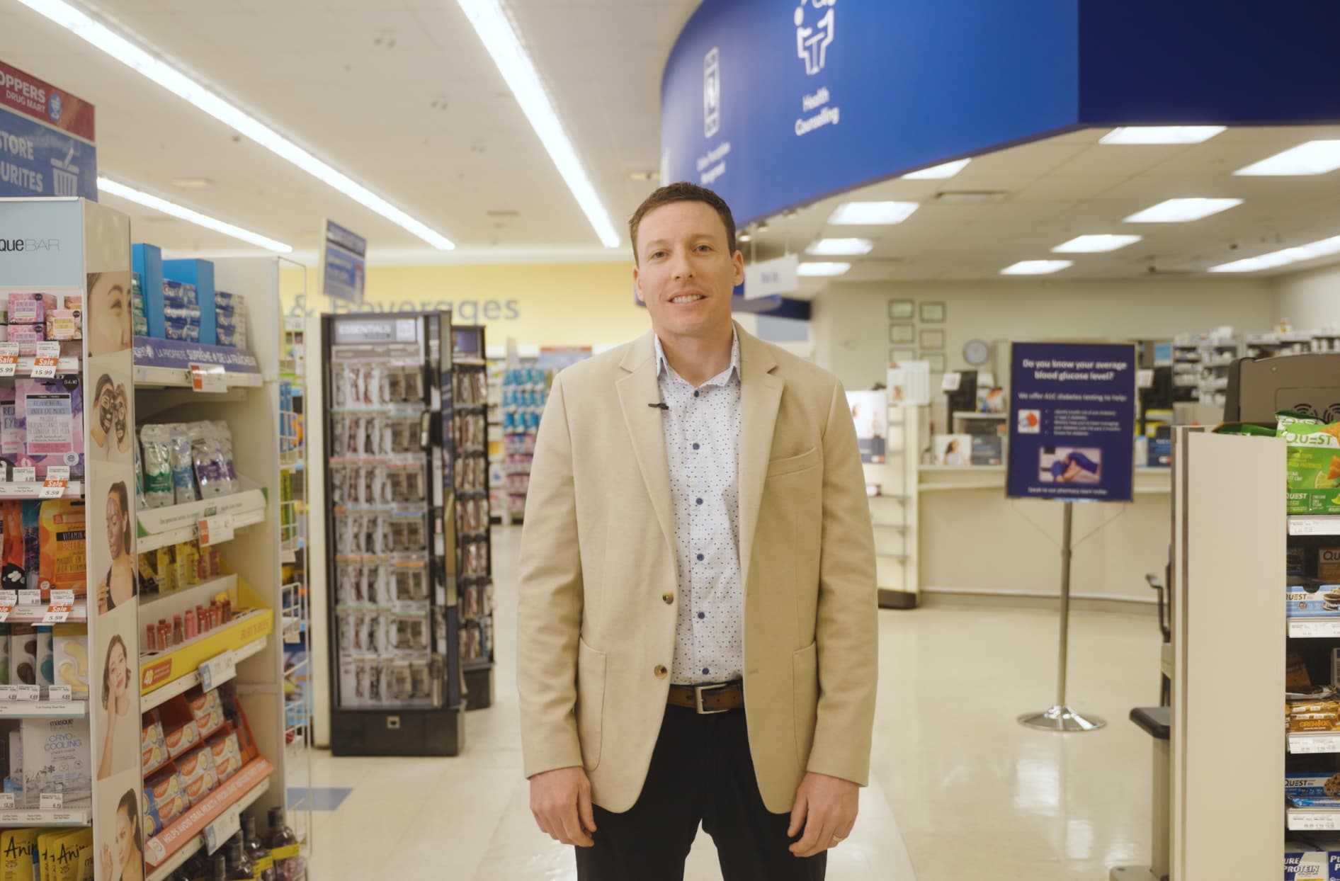 Nathan standing inside of his Shoppers Drug Mart store with shelves behind him in the background.     
